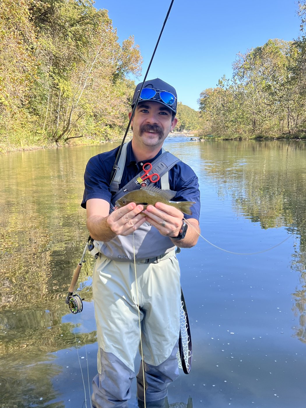 Rhett standing in a river holding a fish he caught on a fly rod